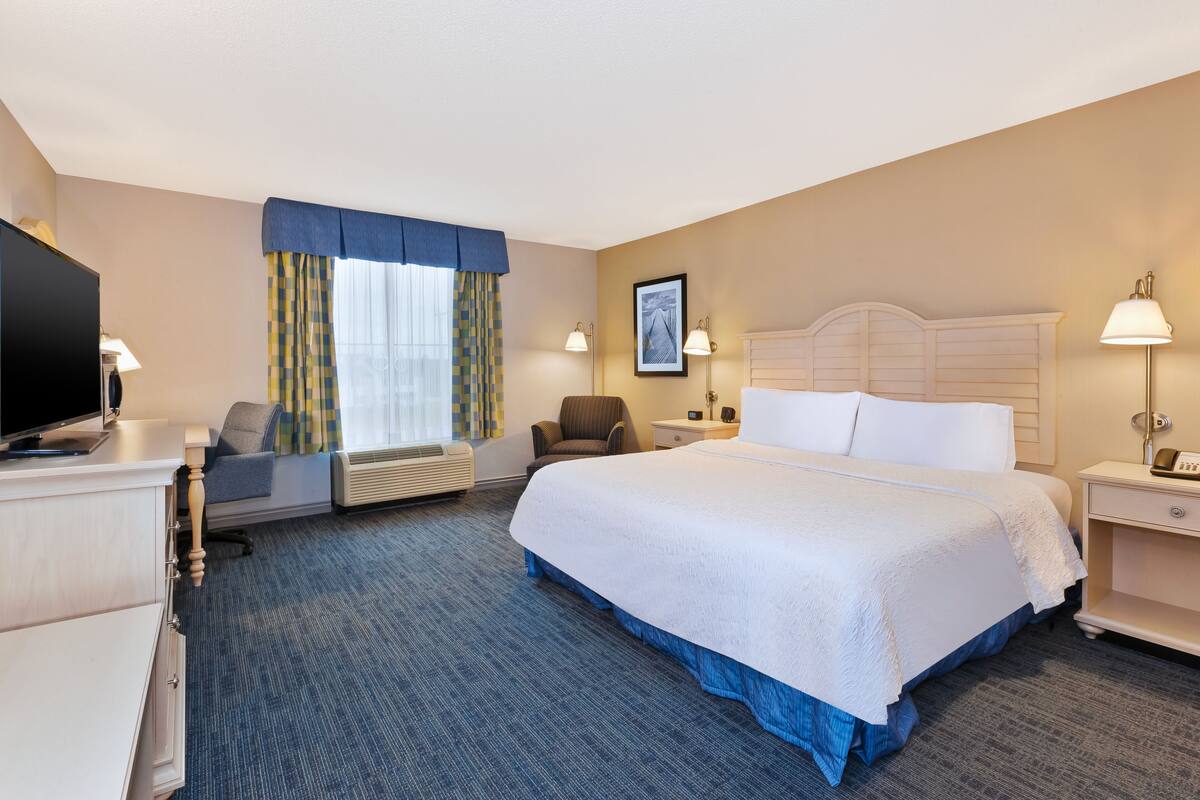 Une chambre d’hôtel avec un grand lit, un bureau avec une télévision, une chaise et une fenêtre avec des rideaux.