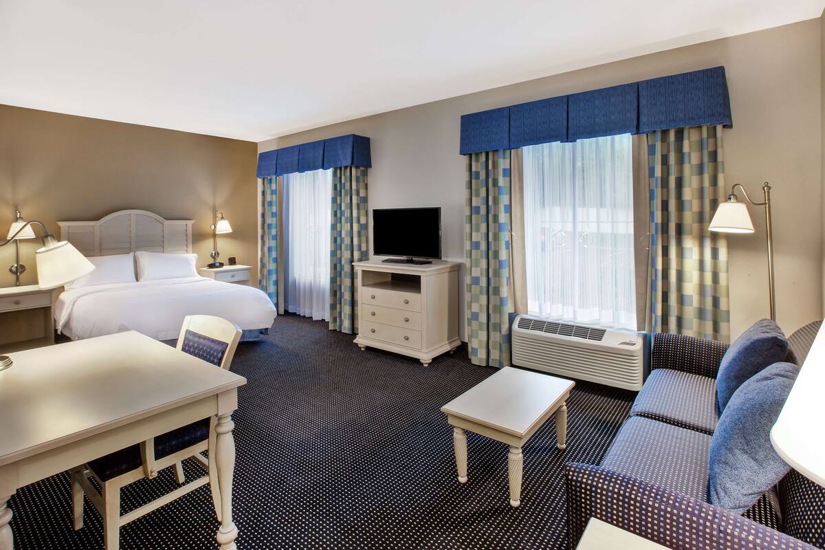 Une chambre d’hôtel avec un lit, un bureau, une télévision, un canapé et une petite table.