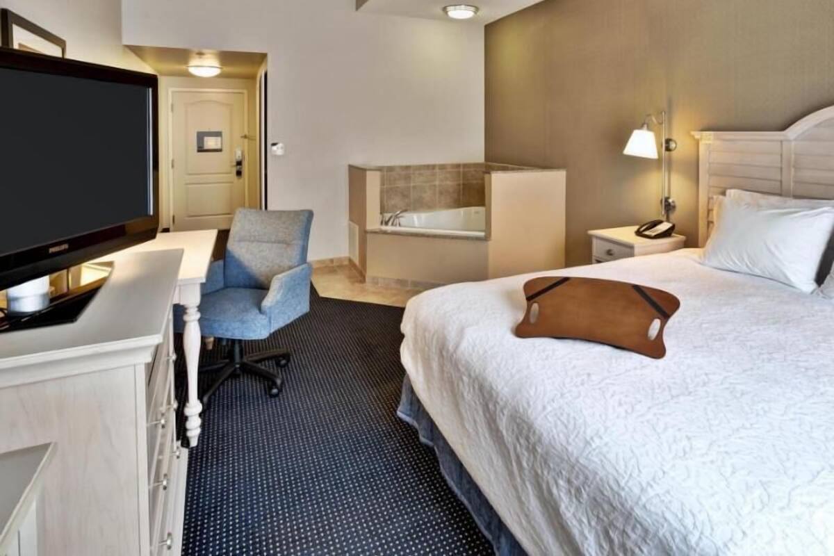 Une chambre d’hôtel comprenant un lit, un bureau avec une télévision, une chaise, une salle de bain avec une baignoire et une table de chevet avec une lampe.