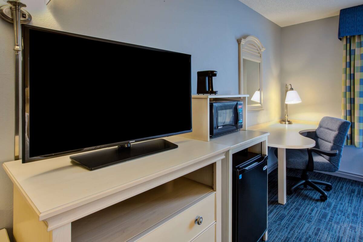 Une chambre d’hôtel équipée d’une télévision à écran plat, d’un four à micro-ondes, d’une machine à café, d’un bureau avec une chaise et d’un petit réfrigérateur.