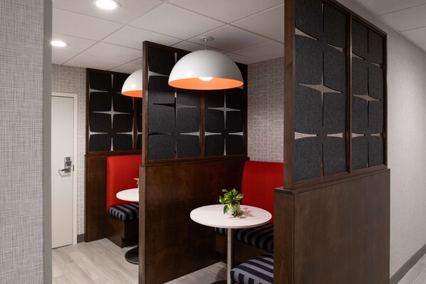 Un interior moderno con una zona de estar que incluye un banco acolchado rojo, una mesa redonda con una planta y un separador con motivos geométricos.