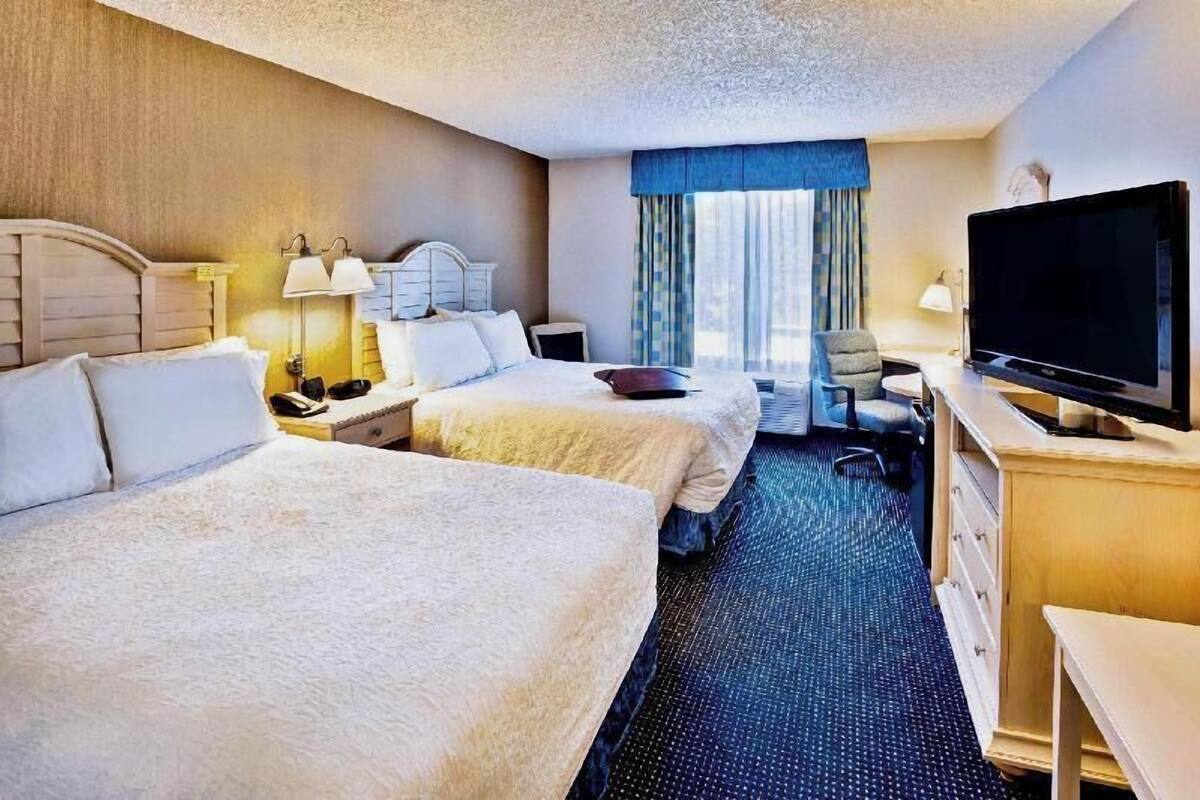 Une chambre d’hôtel avec deux lits, un bureau, une télévision et une fenêtre avec des rideaux.
