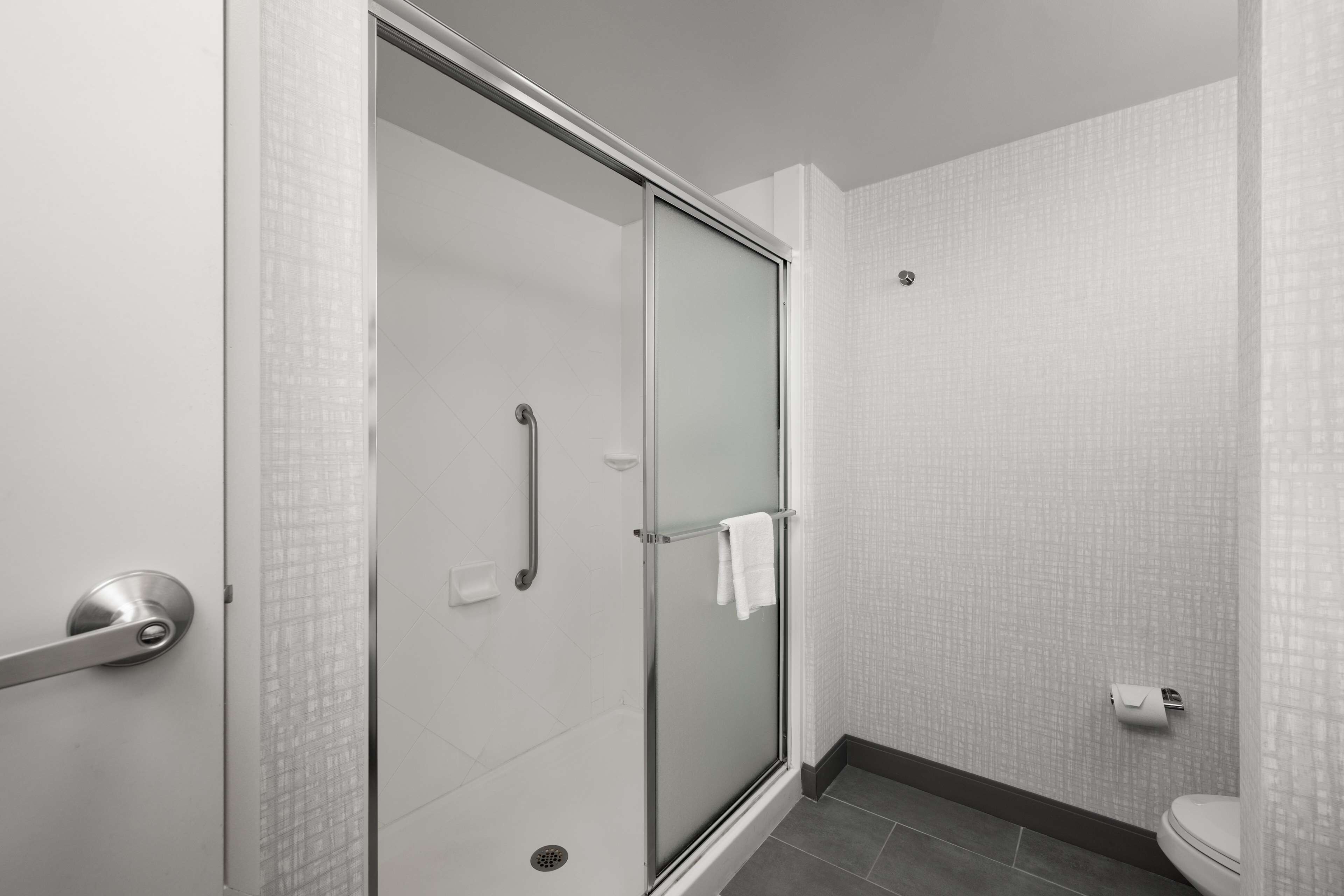 Une salle de bain moderne avec une douche à parois de verre, des toilettes blanches et un sol carrelé.