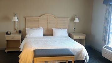 Habitación de hotel con una cama grande, mesitas de noche con lámparas, un banco y un equipo de aire acondicionado.