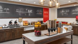 Een ontbijtbuffet met wafelapparaten, een schaal fruit en een koffiehoek.
