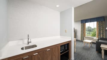 Una cocina moderna con microondas integrado, un lavabo y armarios de madera. Hay una zona de comedor con una mesa y sillas, y una ventana con cortinas.