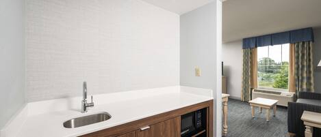 Eine moderne Küche mit integriertem Mikrowellenherd, Spüle und Holzschränken. Ein Essbereich mit Tisch und Stühlen lädt zum Verweilen ein, und ein Fenster mit Vorhängen sorgt für eine gemütliche Atmosphäre.