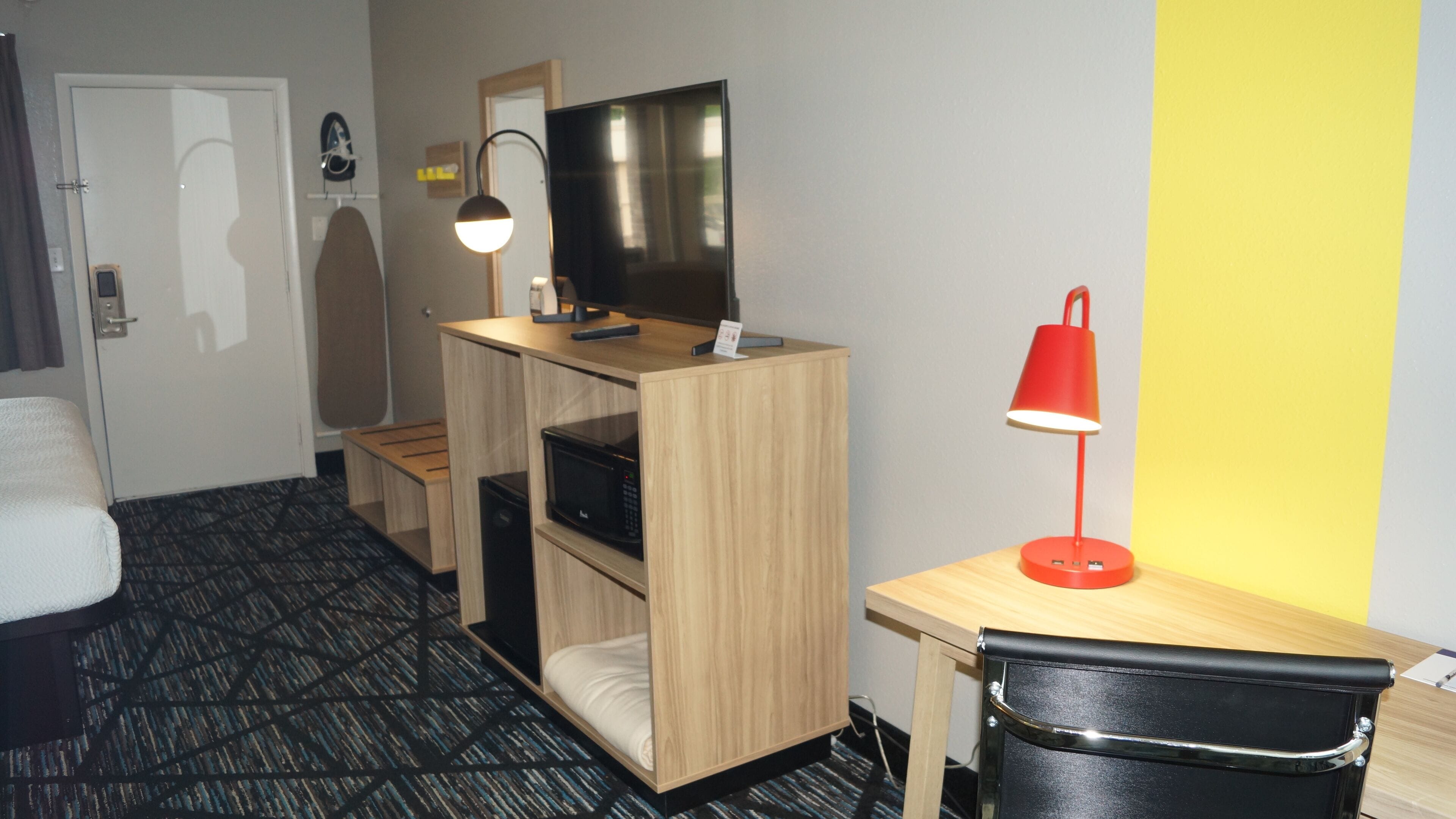 A hotel room with a bed, a desk with a red lamp, a television, and a microwave.
