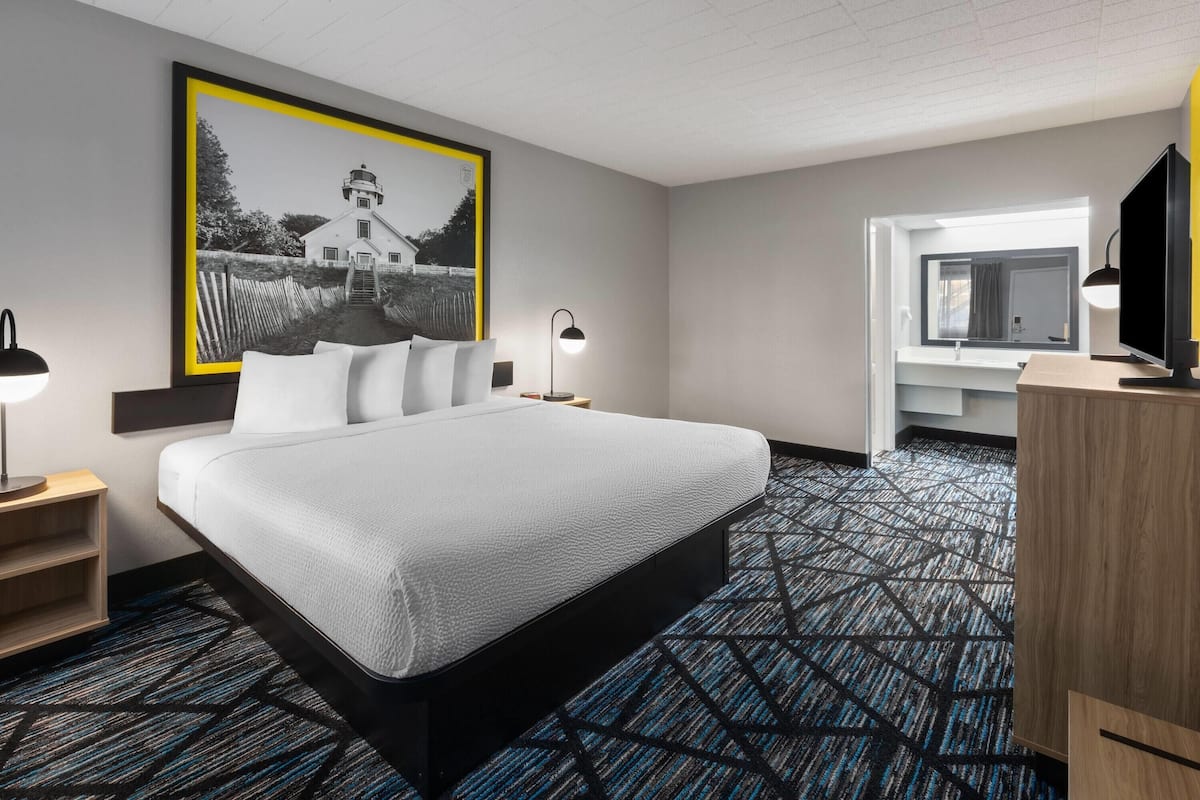 A hotel room with a large bed, a desk with a computer, a TV, and a framed picture on the wall.