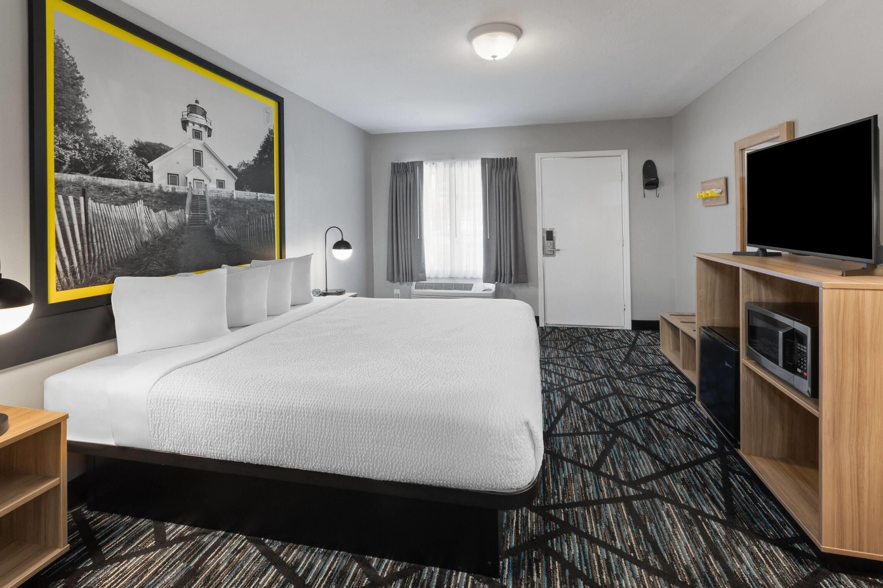 A hotel room with a large bed, a flat-screen TV, a desk with a lamp, a microwave, and a framed picture on the wall.