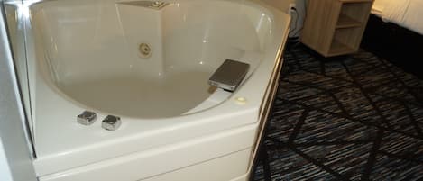 A white bathtub with a control panel, a small wooden side table, and a patterned carpet.