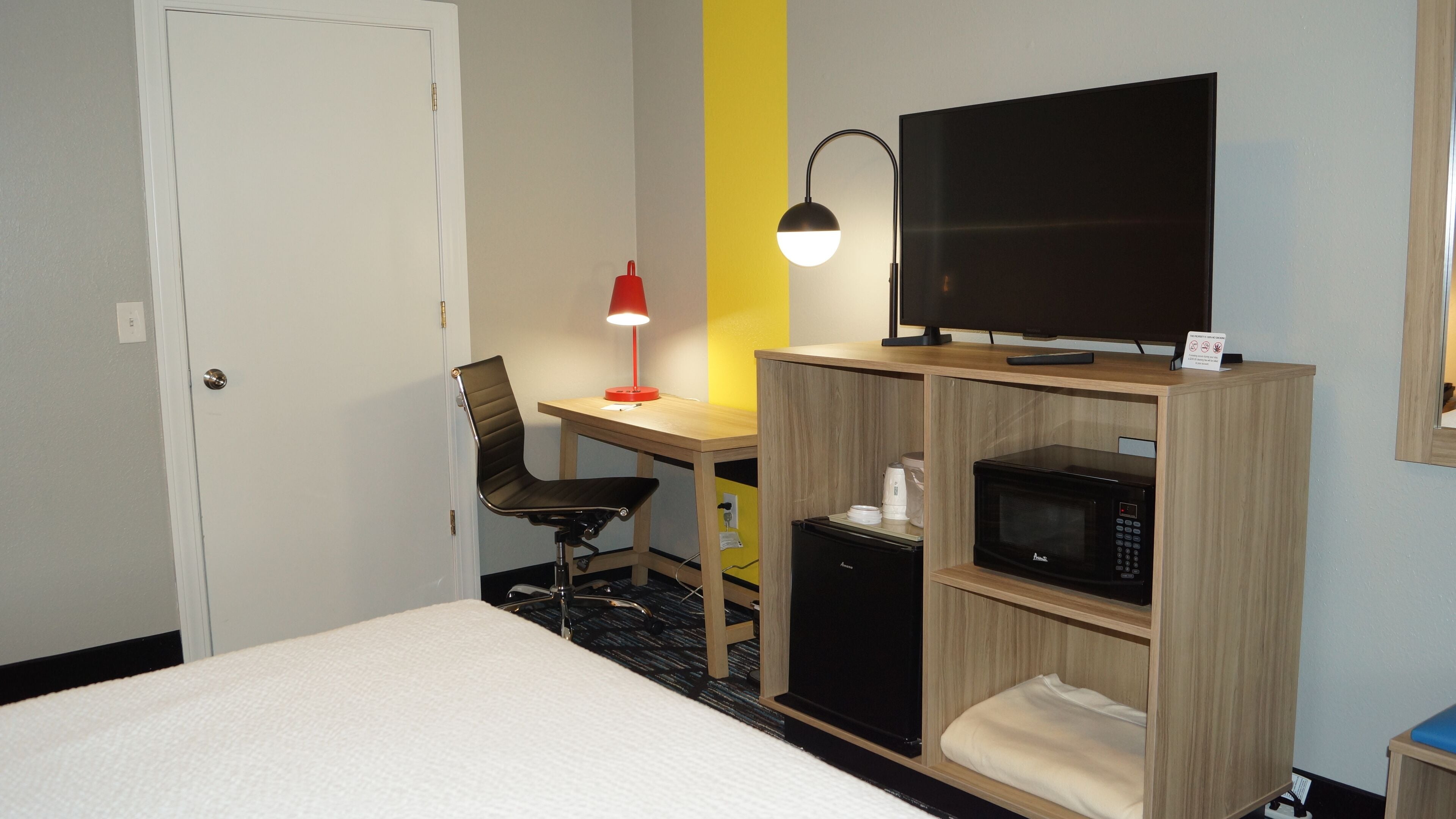 Une chambre d’hôtel équipée d’un lit, d’un bureau avec un ordinateur, d’une télévision, d’un four à micro-ondes et d’une chaise.