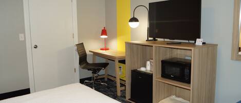 Une chambre d’hôtel équipée d’un lit, d’un bureau avec un ordinateur, d’une télévision, d’un four à micro-ondes et d’une chaise.