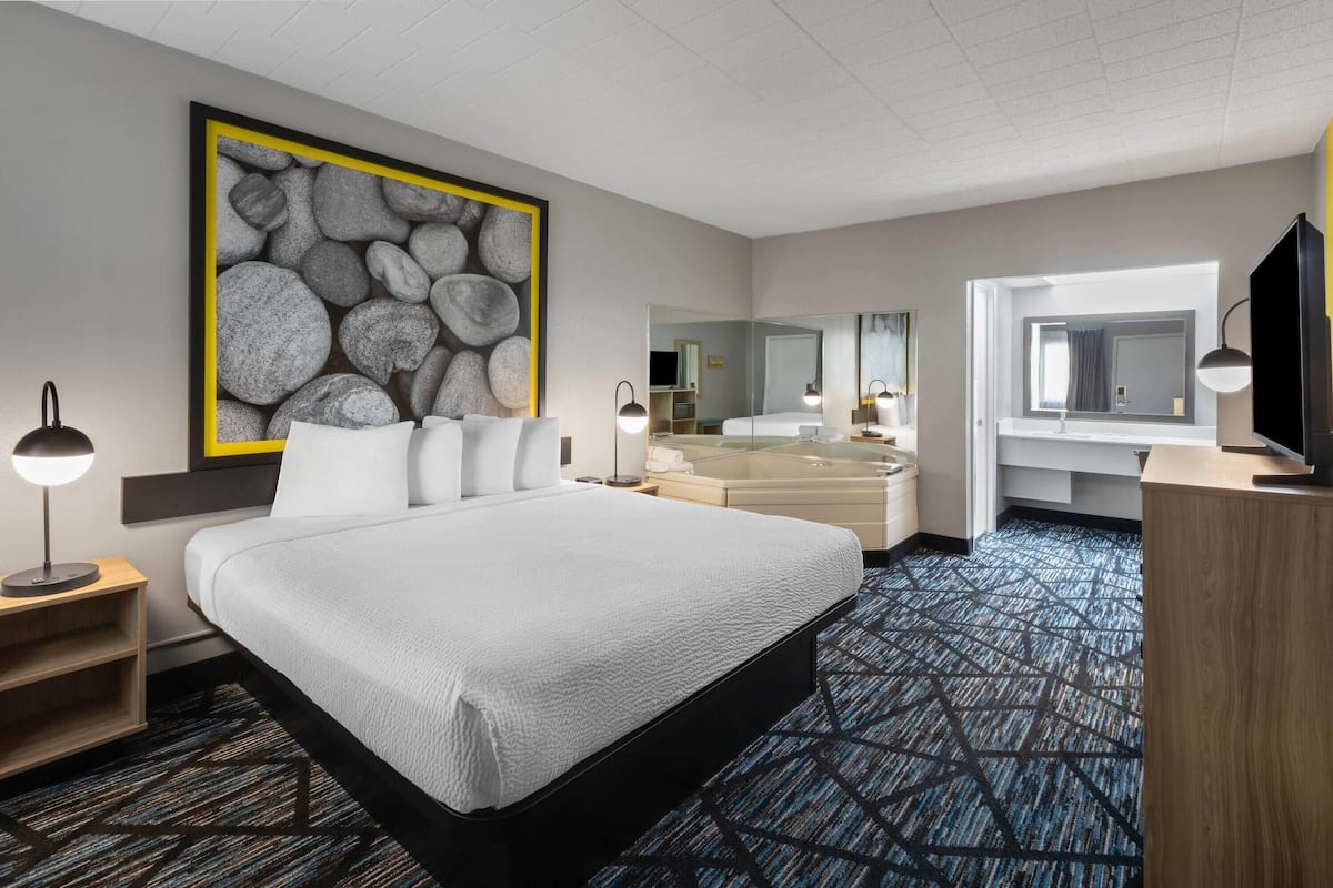 A hotel room with a large bed, a modern bathroom, and a large window.