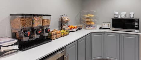 Une petite cuisine équipée d’une machine à café, d’un grille-pain, d’un four à micro-ondes et de divers aliments disposés sur le plan de travail.