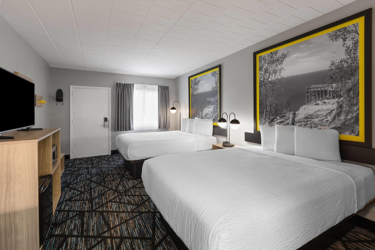 A hotel room with two beds, a TV, a desk, and a large window with curtains.