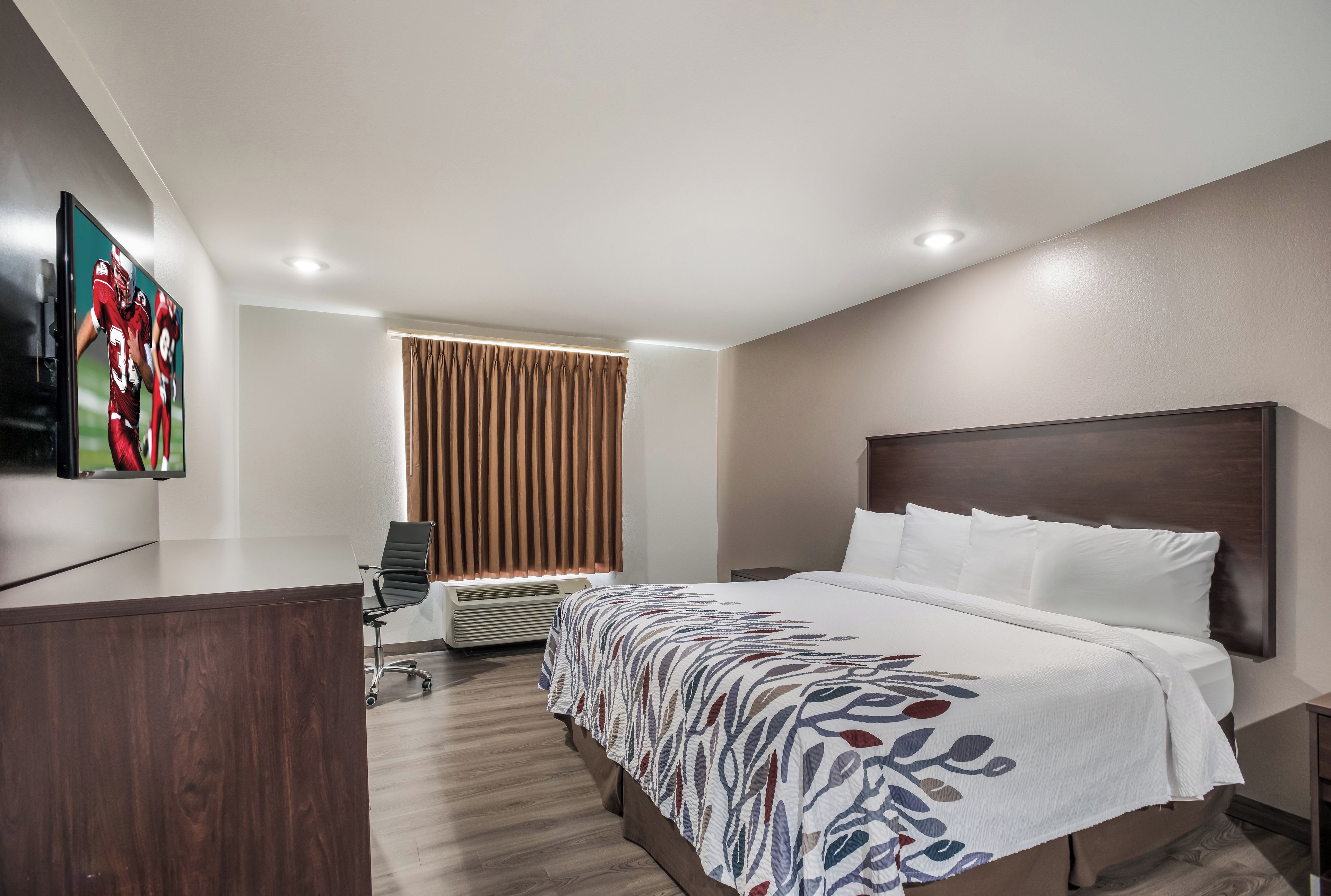A hotel room with a bed, a desk, a chair, a television, and a window with curtains.