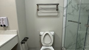 A bathroom with a toilet, a towel rack, a shower with a glass door, and a sink with a countertop.