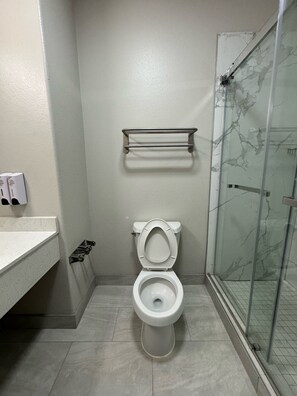 A bathroom with a toilet, a towel rack, a shower with a glass door, and a sink with a countertop. - Red Roof Inn & Suites Lake Charles (Lake Charles)