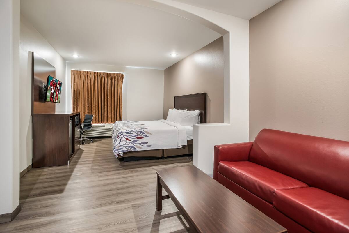 Een hotelkamer met een bed, een rode leren bank, een houten bankje, een bureau met een stoel en een aan de muur bevestigde televisie.