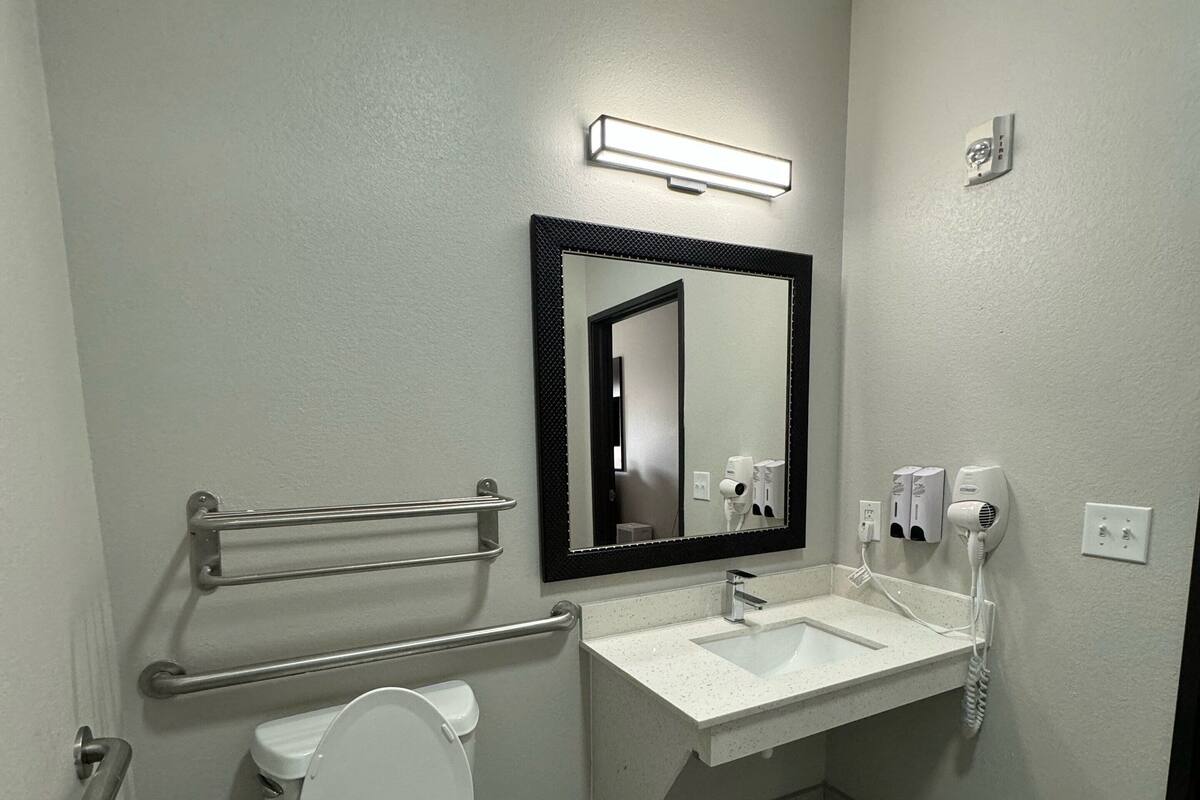 A modern bathroom with a white toilet, a sink with a mirror above it, and a hand dryer.