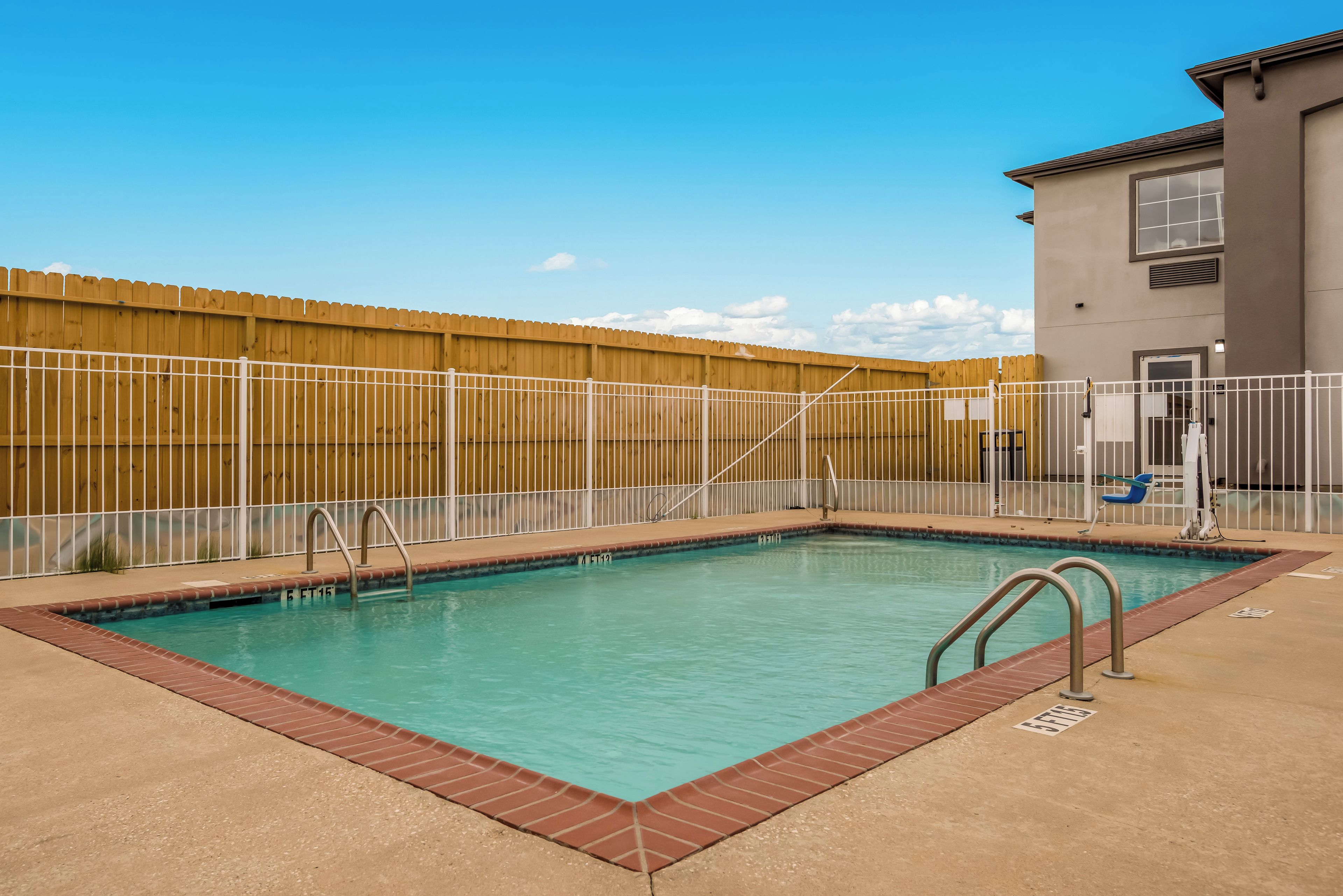 A rectangular pool with a wooden fence and metal railings, surrounded by a concrete deck.