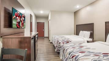 Habitación de hotel con cama, escritorio, silla, televisor montado en la pared y puerta.