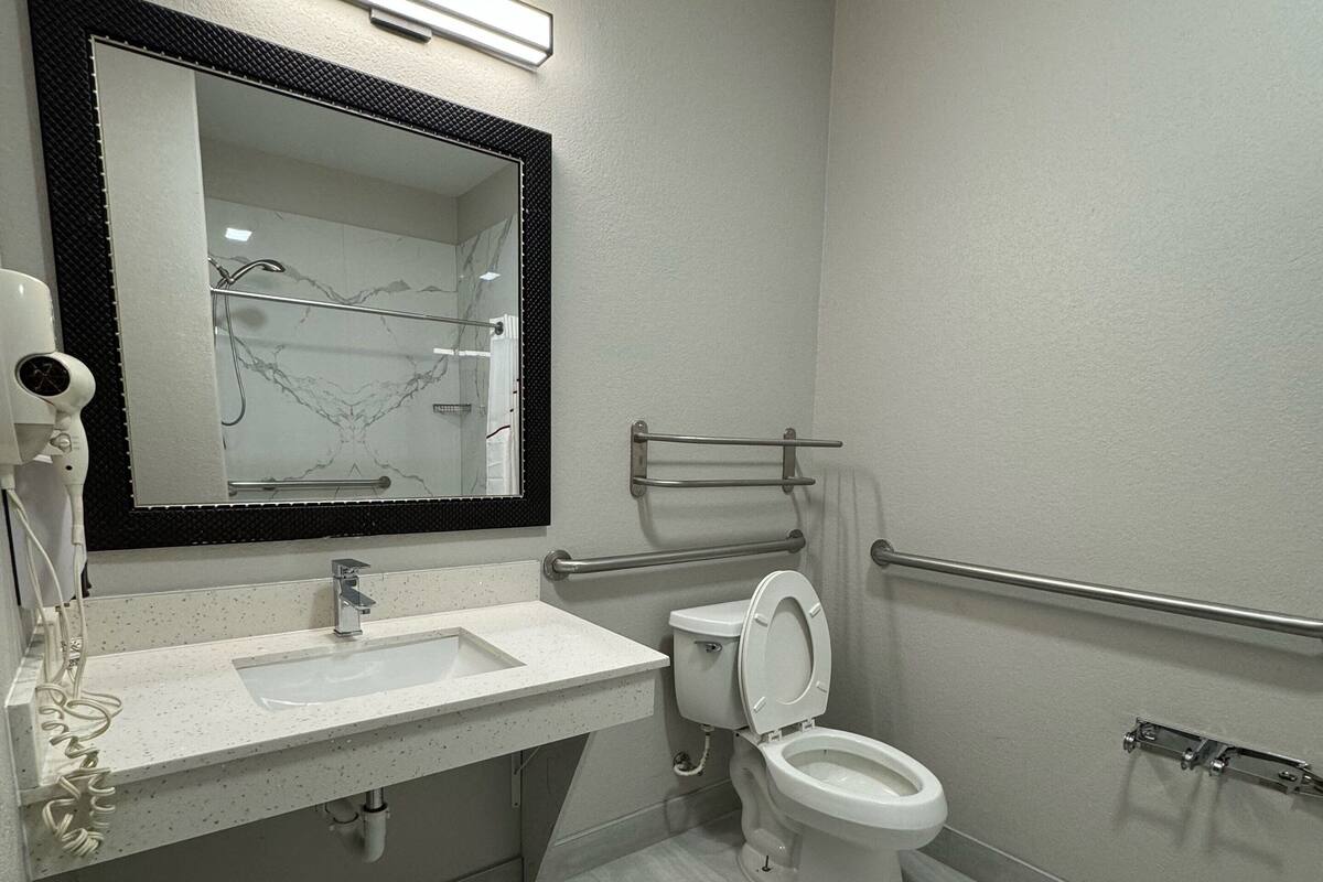 A modern bathroom with a white sink, a mirror, a toilet, and a shower area.