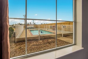 A view of a swimming pool with a fenced area, a wooden deck, and a clear sky. - Red Roof Inn & Suites Lake Charles (Lake Charles)