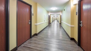 Un couloir d’hôtel avec des portes en bois, des murs de couleur claire et un sol à motifs.