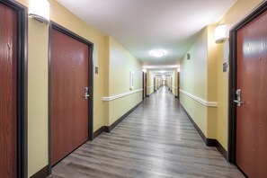 Un couloir d’hôtel avec des portes en bois, des murs de couleur claire et un sol à motifs.