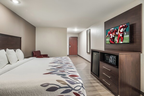 A hotel room with a large bed, a TV mounted on the wall, a wooden cabinet, and a door leading to another room.