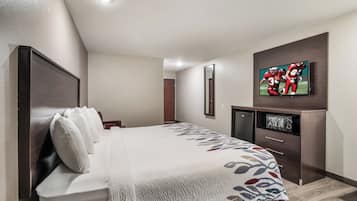 A hotel room with a bed, a television mounted on the wall, a small cabinet, and a door leading to another room.