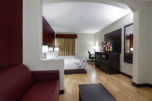A hotel room with a bed, a desk, a TV, a red sofa, and a wooden floor. - Red Roof Inn & Suites Lake Charles (Lake Charles)