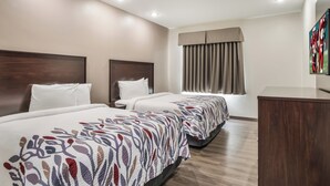 A hotel room with two beds, a wooden headboard, a large window with curtains, and a flat-screen TV mounted on the wall.