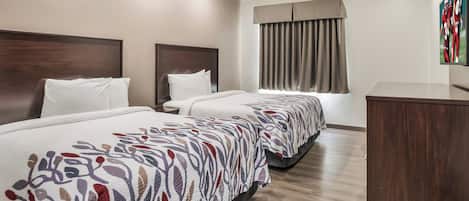 Habitación de hotel con dos camas, cabecero de madera, un ventanal con cortinas y un televisor de pantalla plana montado en la pared.