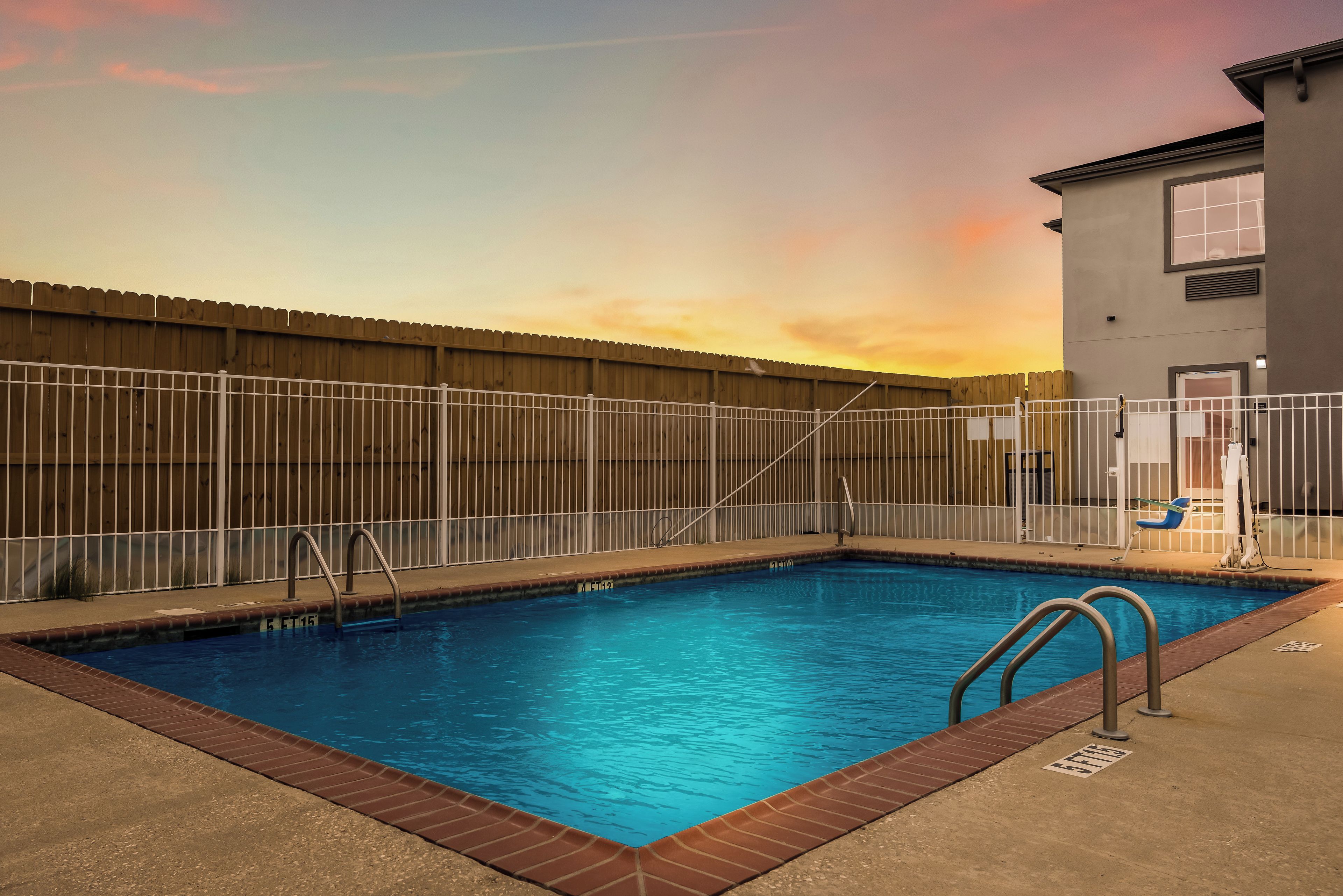 A rectangular swimming pool with a wooden fence, metal pool ladder, and a clear blue sky in the background.