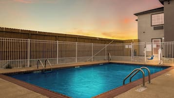 A rectangular swimming pool with a wooden fence, metal pool ladder, and a clear blue sky in the background.