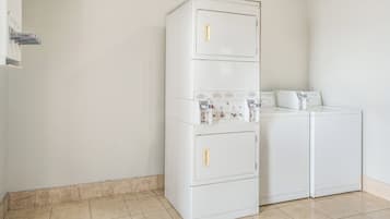 Un lavadero pequeño con una lavadora y secadora apiladas, altas y de color blanco, además de una lavadora y secadora más pequeñas.