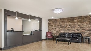 Un área de recepción con un mostrador oscuro, una silla roja, un sofá de cuero y una pared de piedra.