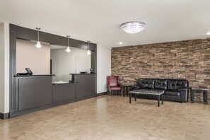 A reception area with a dark counter, a red chair, a leather sofa, and a stone wall. - Red Roof Inn & Suites Lake Charles (Lake Charles)