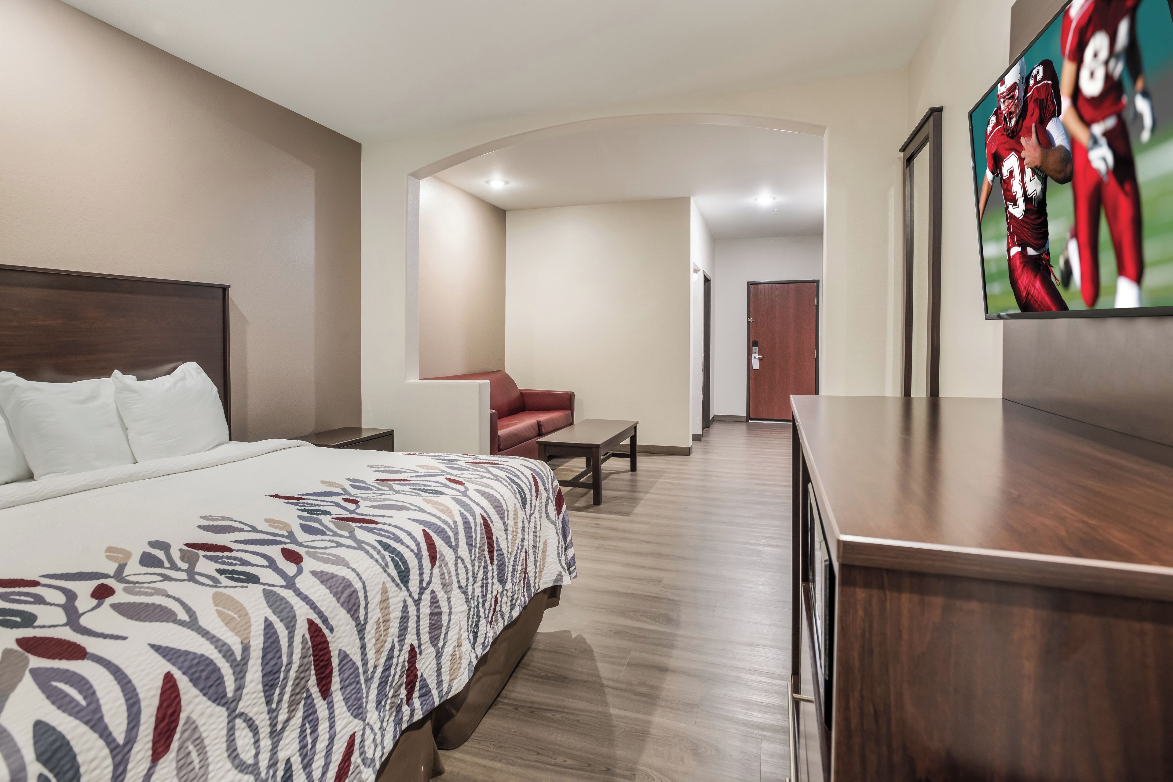 Une chambre d’hôtel avec un grand lit, un bureau, une chaise et un téléviseur diffusant un événement sportif.