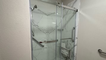 A modern bathroom with a glass-enclosed shower, marble walls, and a tiled floor.