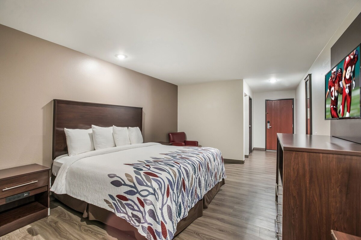 A hotel room with a large bed, a wooden headboard, a desk, and a television on the wall.