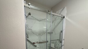 A modern bathroom with a glass-enclosed shower, marble walls, and a tiled floor.