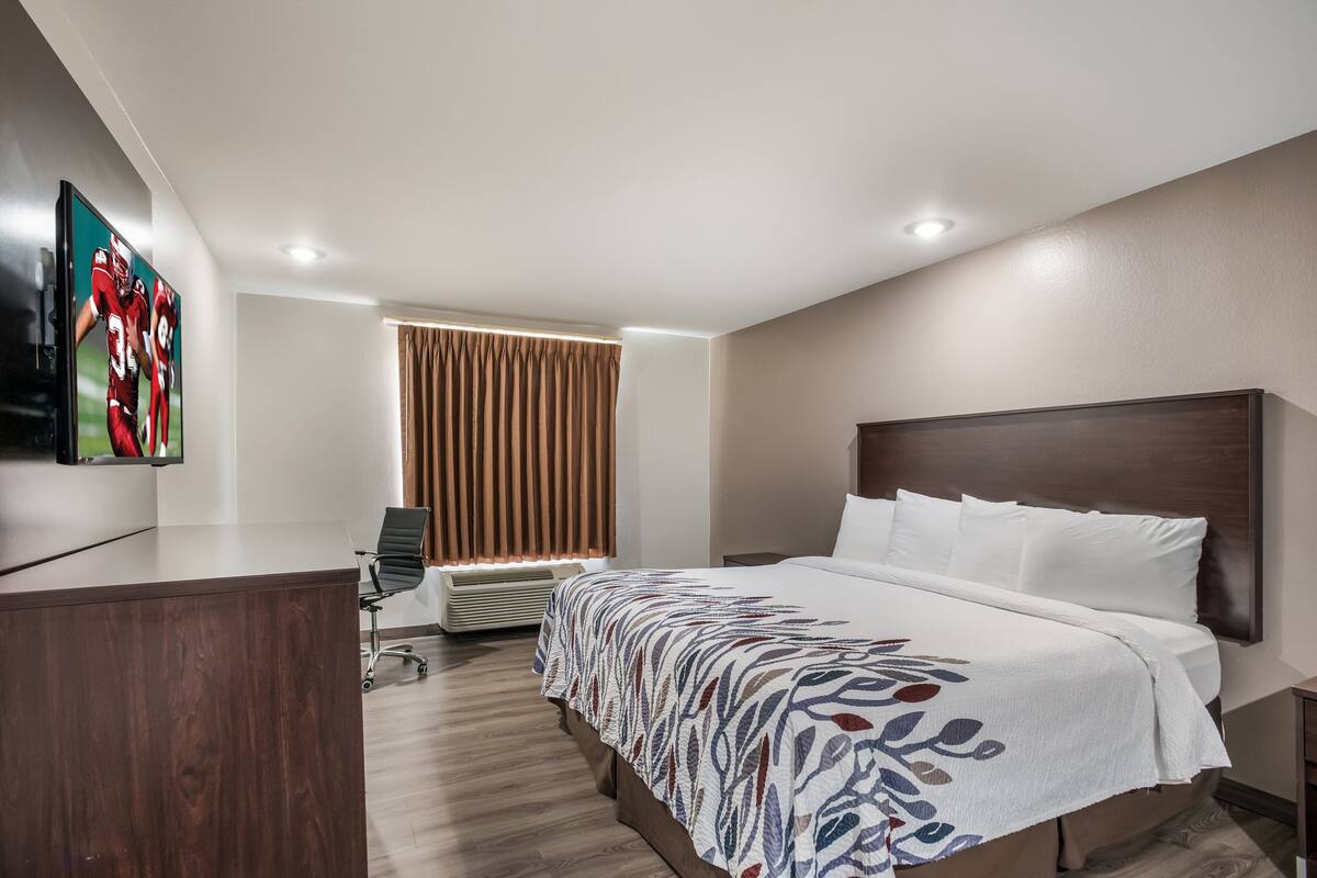 Een hotelkamer met een groot bed, een bureau, een stoel, een flatscreen televisie en een raam met gordijnen.