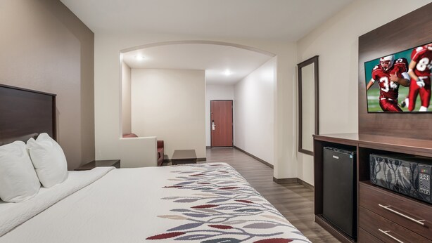 A hotel room with a large bed, a flat-screen TV mounted on the wall, a refrigerator, and a microwave.