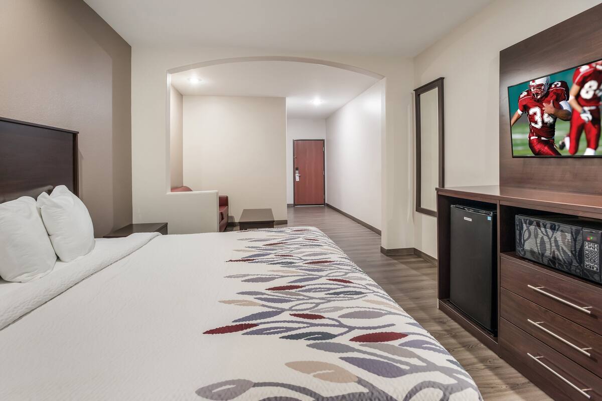 A hotel room with a large bed, a flat-screen TV mounted on the wall, a refrigerator, and a microwave.