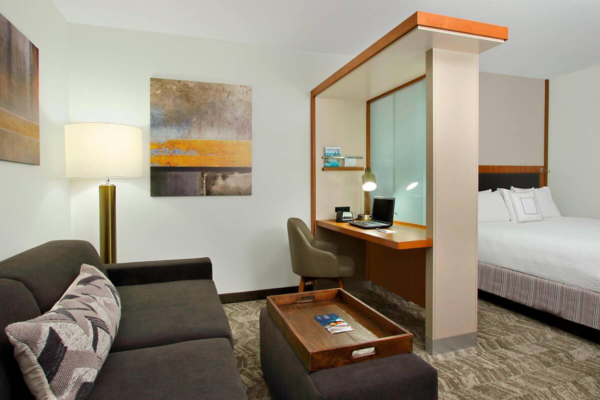 Una habitación de hotel con una cama, un escritorio con computadora, una silla, un sofá y una mesa de centro.