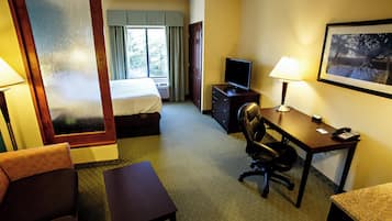 A hotel room with a bed, desk, chair, television, and a painting on the wall.